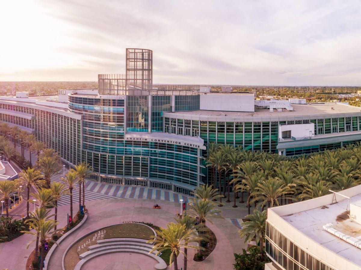 A large, modern building with glass and palm trees, seen from above, under a clear sky at sunset or sunrise.