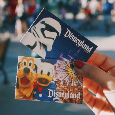 A hand reaching to grab a small yellow toy or figure in front of a blue plastic container, with a crowd blurred in the background.