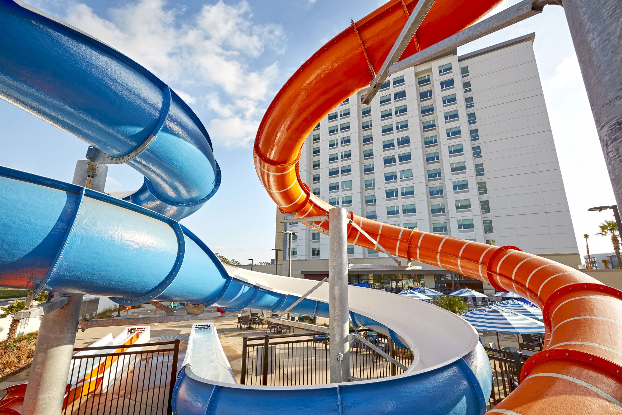 Water slides twist and turn by a hotel pool, blue and orange tubes curve against a tall building. End.